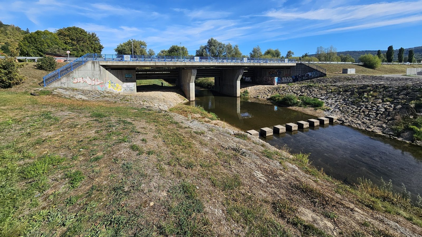 Die Rems unterhalb der Brücke Ostlandstraße heute: kahle Böschung links, Steinschüttung rechts, Trittsteine, Graffiti an den Widerlagern